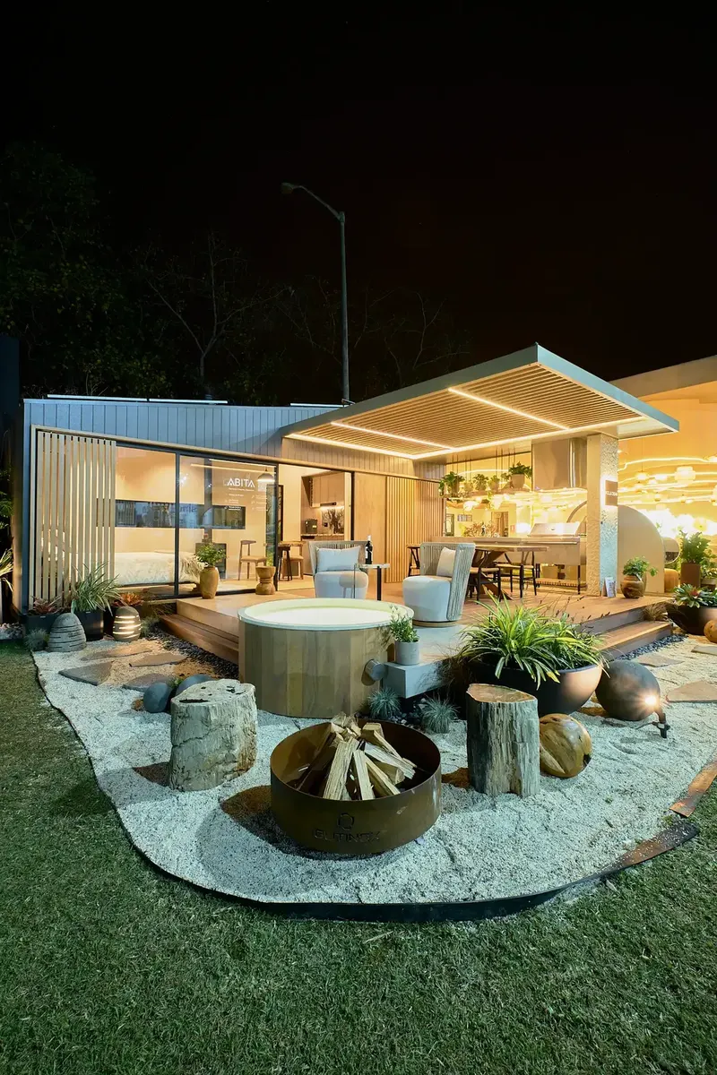 Casa Modular ABITA iluminada de noche en Expodeco 2025, con fogón y jardín de grava